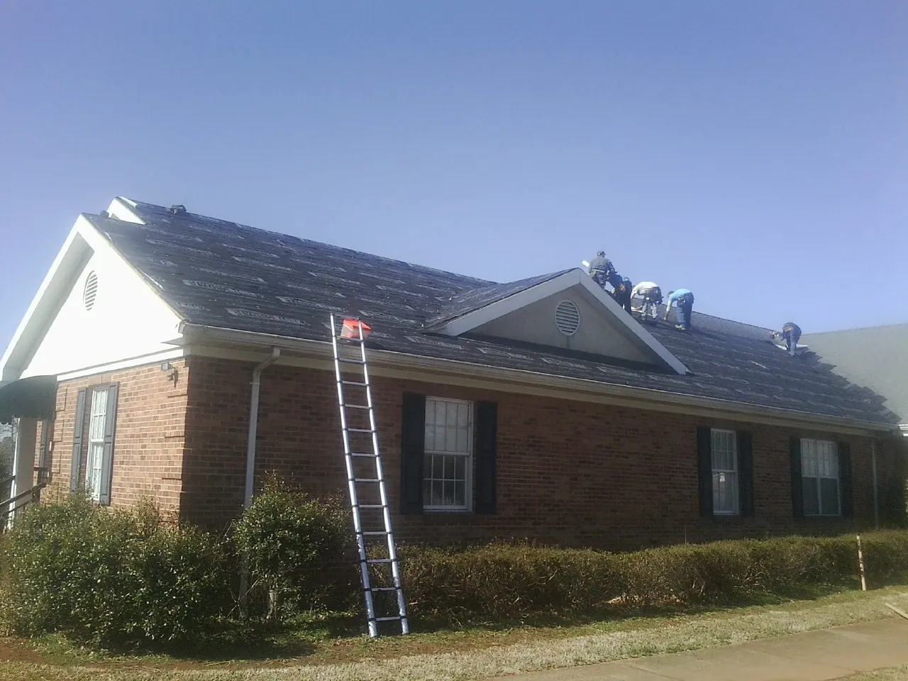 Crew tearing shingles off a brick ranch roof with a ladder set — Metal Roof Repair work by our crew in Arock
