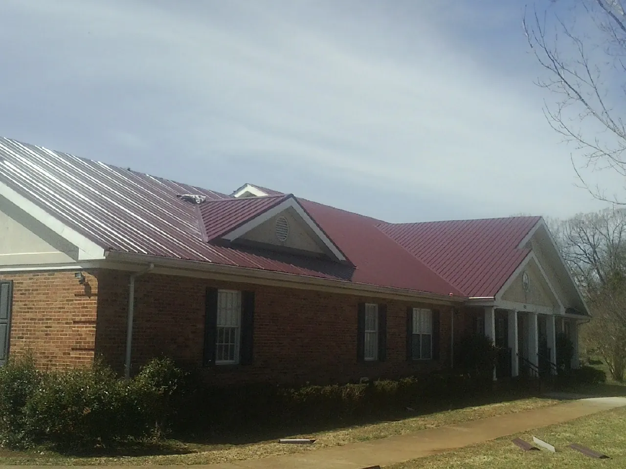 Red metal roof with gabled entries on a long brick building, from a Hail Damage Roof Repair job in Arock