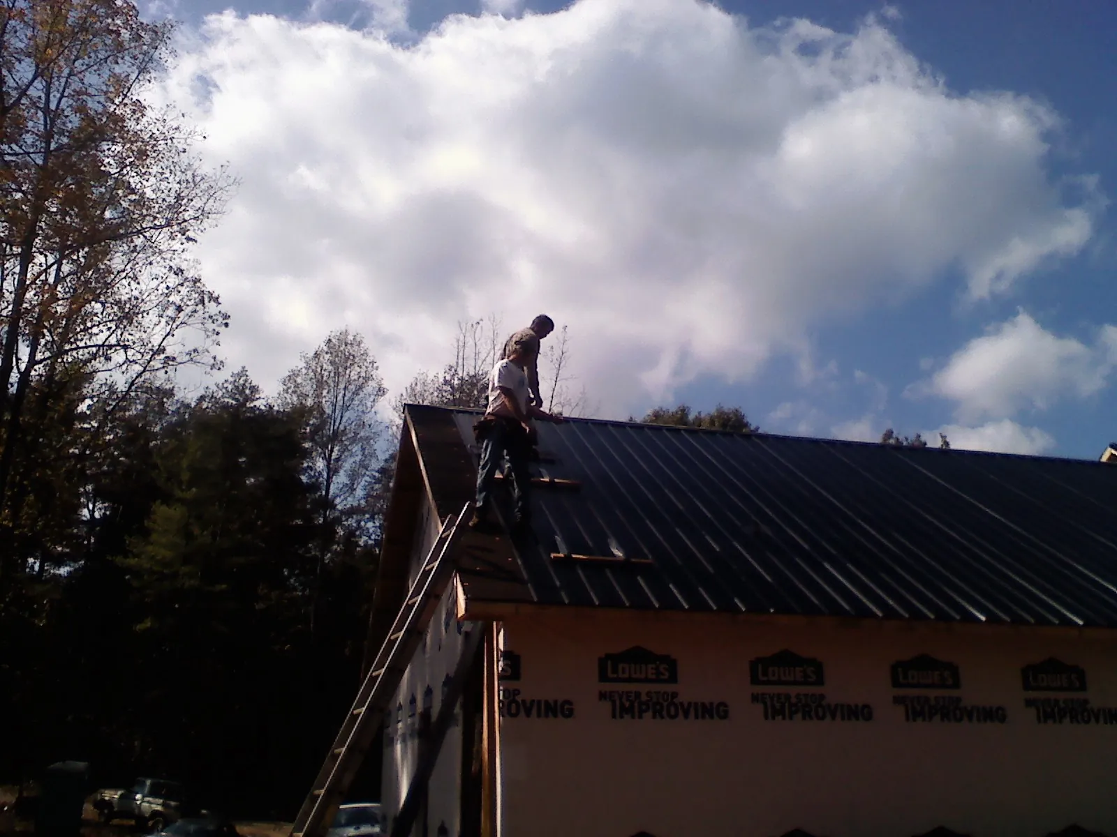 Roofer fastening dark metal panels high against a cloudy sky, from a Roof Inspection job in Arock