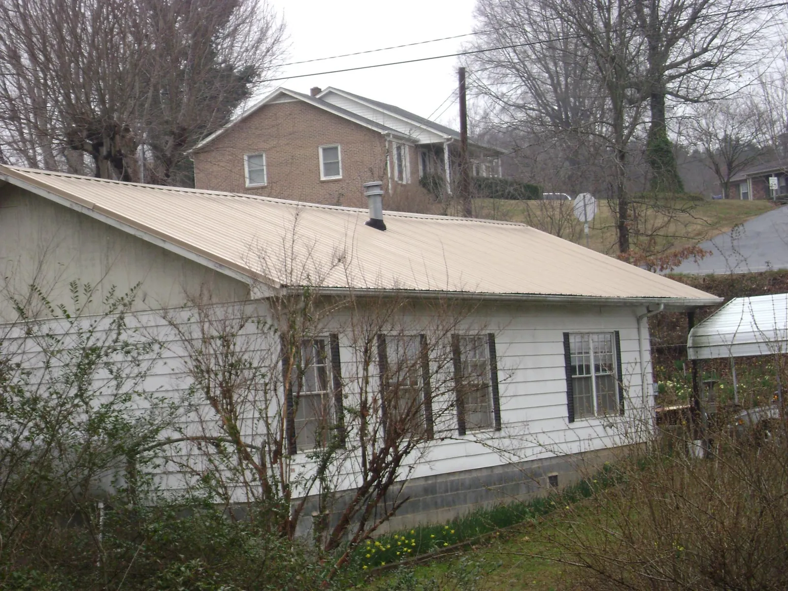 Tan metal roof on a white sided house set into a hillside — Commercial Roofing by Roofing Brothers in Arock